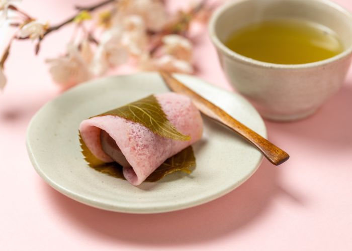 A seasonal sakura mochi, featuring pink mochi wrapped with a cherry blossom leaf.